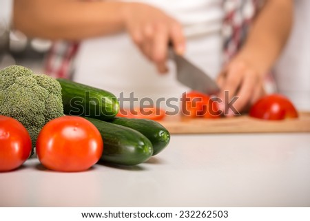 Close-up hands of a woman who cuts vegetables. Focus on the vegetables on the table.