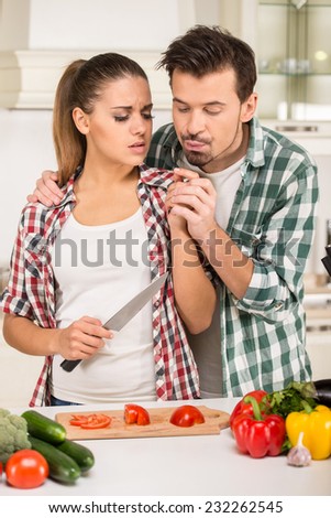 Beautiful young couple in the kitchen while cooking. Woman injured a finger.