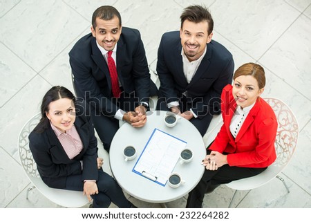 Top view of several business people are planning work at round table. They are looking at the camera.