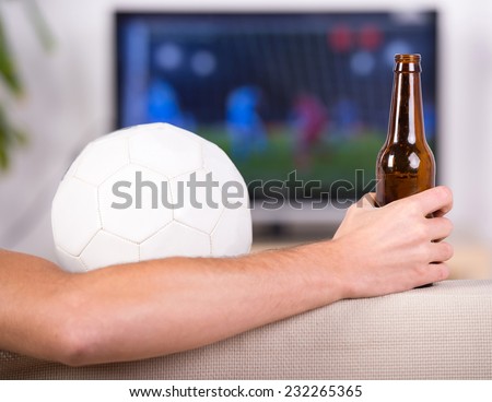 Close-up soccer ball and hand with a beer, man who looks a soccer match.