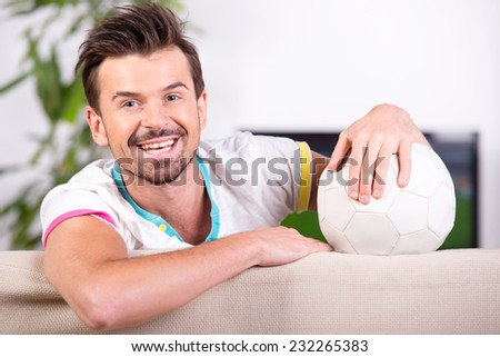 Smiling young man with soccer ball while watching the game. Looking at the camera.