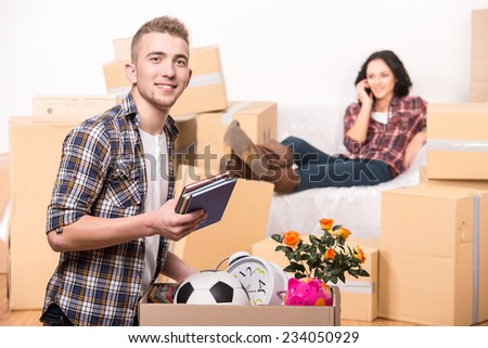 Woman in a new home with cardboard boxes, is sitting on covered sofa and speaking by phone. Man is looking at the camera.