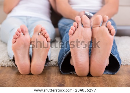 Close-up feet of young woman and man are sitting on the floor.