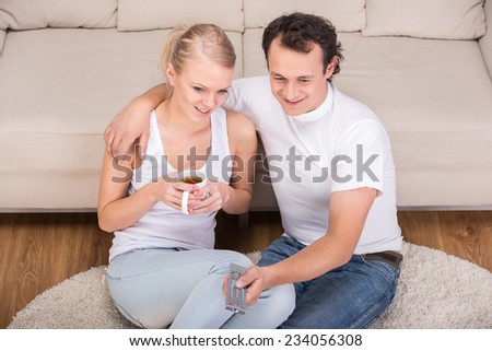 Young couple are spending time together. They drink tea and watch TV.