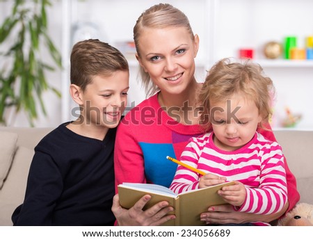 Young mother and her two children are reading a book together. Happy family.
