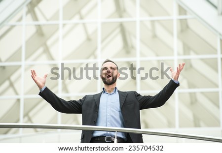 Happy young business man at work in modern office, raised his hands up.