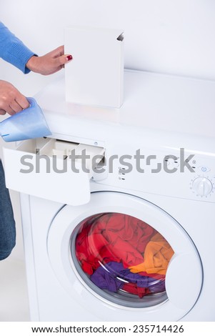 Hands of woman is doing laundry with washing machine at home.