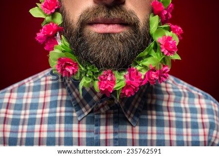 Close-up of man with flowers in his beard is standing against red background.