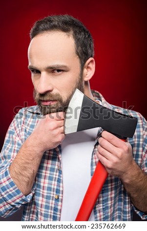 Confident, brutal bearded man with big axe on a red background.