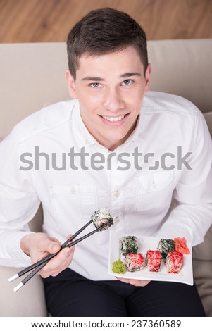 Man enjoying sushi. Cheerful young man is eating sushi and looking at the camera. Top view.