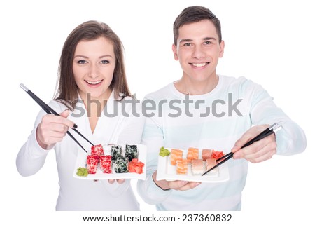 Eating sushi together. Beautiful couple are eating sushi while standing on white background.