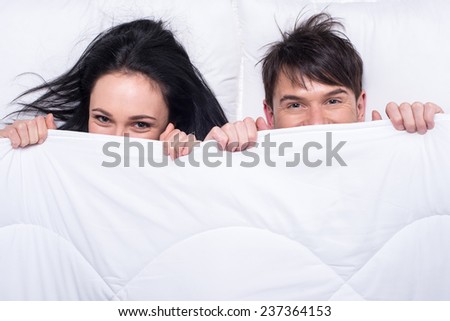 Young happy couple in a bed. Top view. They are looking at the camera.