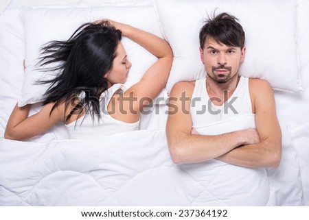 Young woman is sleeping in the bed. Husband is looking at camera.