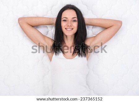 Young, smiling woman is lying on the bed. Quality mattress.