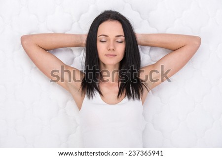 Young, beautiful woman is lying on the bed. Quality mattress.