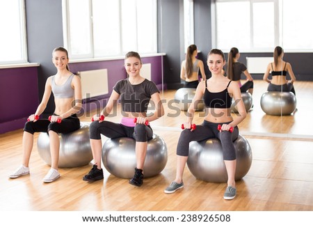Fitness, sport, training and lifestyle concept - three smiling woman with exercise balls and dumbbells in gym.