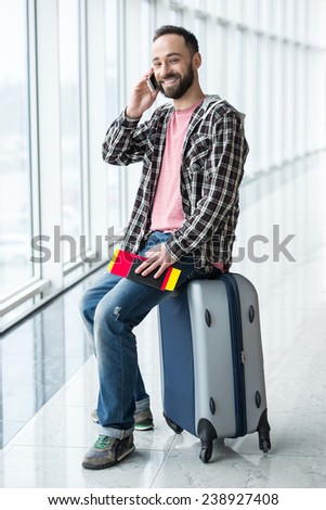 Young man with a suitcase and passport ready to travel. He is speaking by phone.