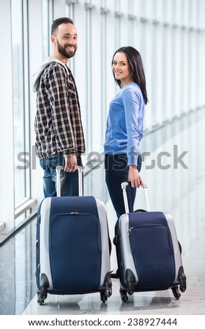 Beautiful couple with luggage bags at airport are looking at the camera.