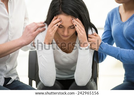 Feeling pain and depression. Depressed young woman is sitting at the chair while other people are comforting her.