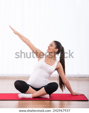 Portrait of pretty pregnant woman is practicing physical exercise over white background.