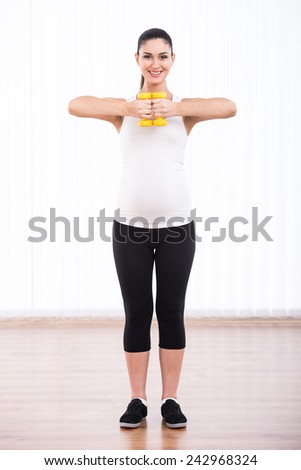 Beautiful, smiling pregnant woman is doing sport with dumbbells, isolated on white background.