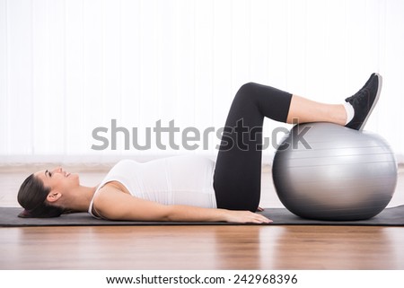 Pregnant woman is doing exercises with gymnastic ball. White background.