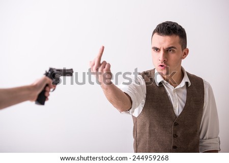 Hand is holding a gun and man with finger up. Grey background.