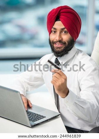 Indian businessman with laptop and credit card is looking at the camera.