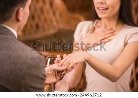 Man is making proposal with the ring to his girlfriend at the restaurant. Shocked and surprised woman.