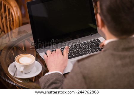 Back view of man with laptop and coffee at cafe.