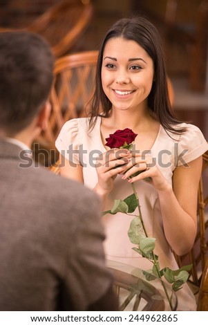 Young happy couple romantic date at restaurant, man gave red rose to his girl.