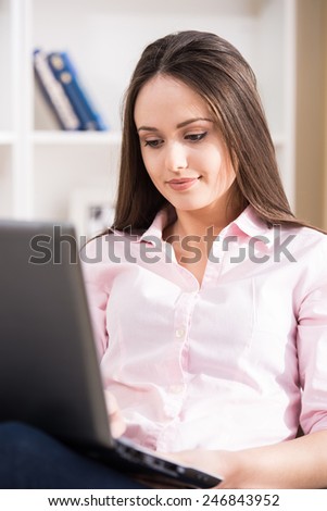 Casual young woman is using laptop while sitting on couch at home.