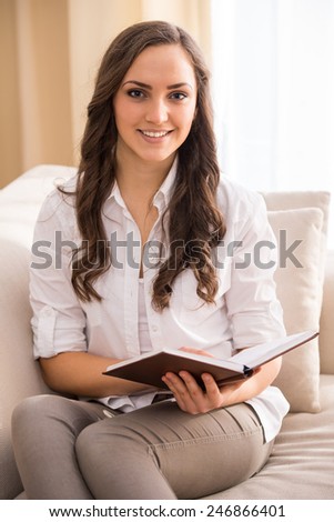 Young woman is reading a book on the couch.