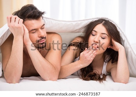Young couple under the covers in bed are yawning.