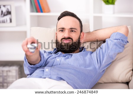 Young man is relaxing at home, using a control remote while watching tv.