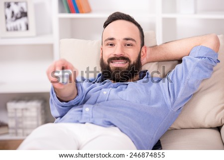 Young man is relaxing at home, using a control remote while watching tv.