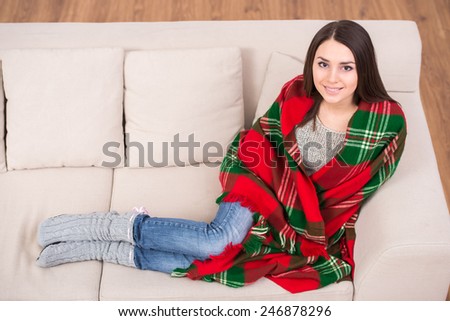 Top view of beautiful young girl sitting on sofa at home wrapped a blanket.