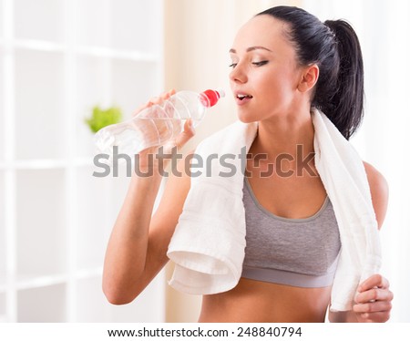 Fitness, home and diet concept. Smiling young woman with bottle of water after exercising at home.