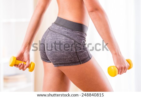 Young woman is exercising with dumbbells at home. Fitness, workout, healthy living and diet concept.