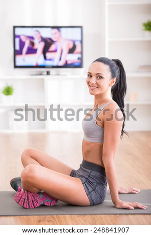 Fitness at home concept. Smiling young woman is sitting on mat at home.