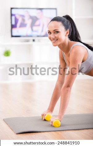 Woman is doing fitness at home on her living room floor while watching and participating in a class. She is looking at the camera.