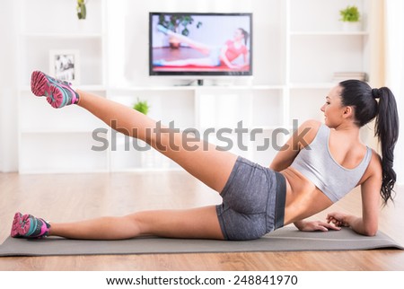 Fitness, workout, healthy living and diet concept.  Rear view of young woman is stretching on floor and watching tv at home.