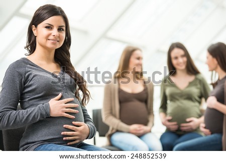 Beautiful pregnant woman is looking at the camera. Happy pregnant women are talking together at antenatal class at the hospital on background.