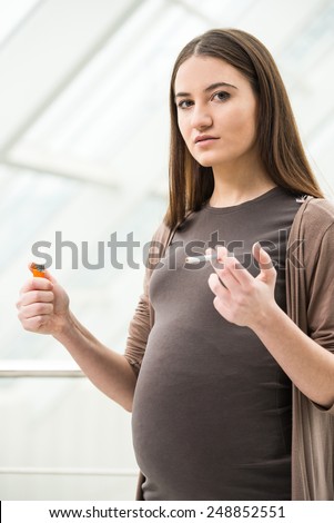 Young pregnant is holding a cigarette. Unhealthy. Pregnant woman is smoking.