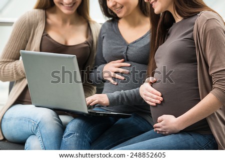Close-up of three pregnant women are watching something interesting over internet.