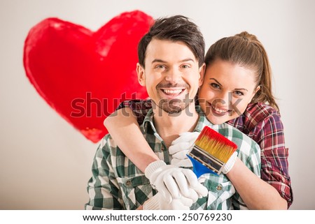 Portrait of young happy couple painted a heart on the wall while doing repair at home and looking at the camera.