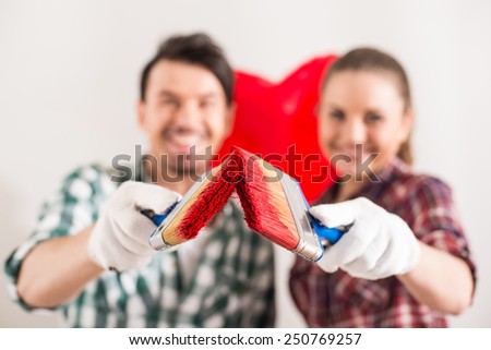 Portrait of young happy couple painted a heart on the wall while doing repair at home and looking at the camera.