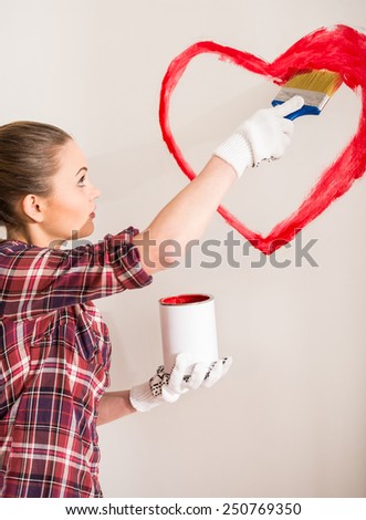 Young woman with paintbrush is drawing a heart on the wall.