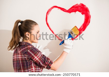 Young woman with paintbrush is drawing a heart on the wall.