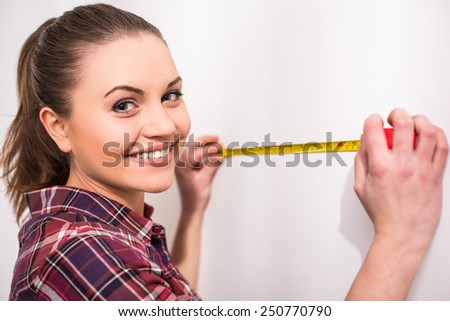 Repair home concept. Young woman is measuring a wall with measuring tape.
